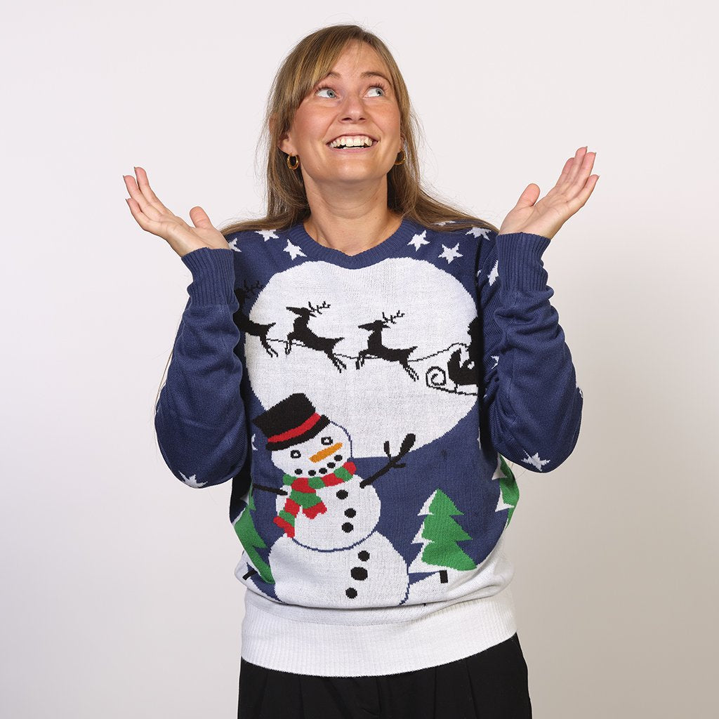 Una donna che indossa un maglione natalizio blu con un pupazzo di neve e una luna.